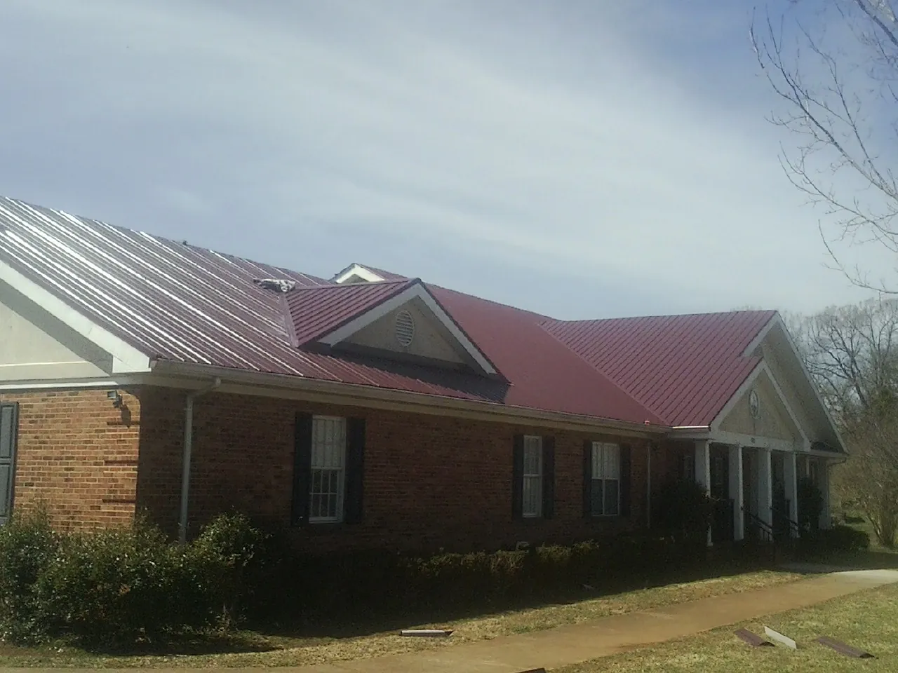 Red metal roof with gabled entries on a long brick building, from a Hail Damage Roof Repair job in Blacklick