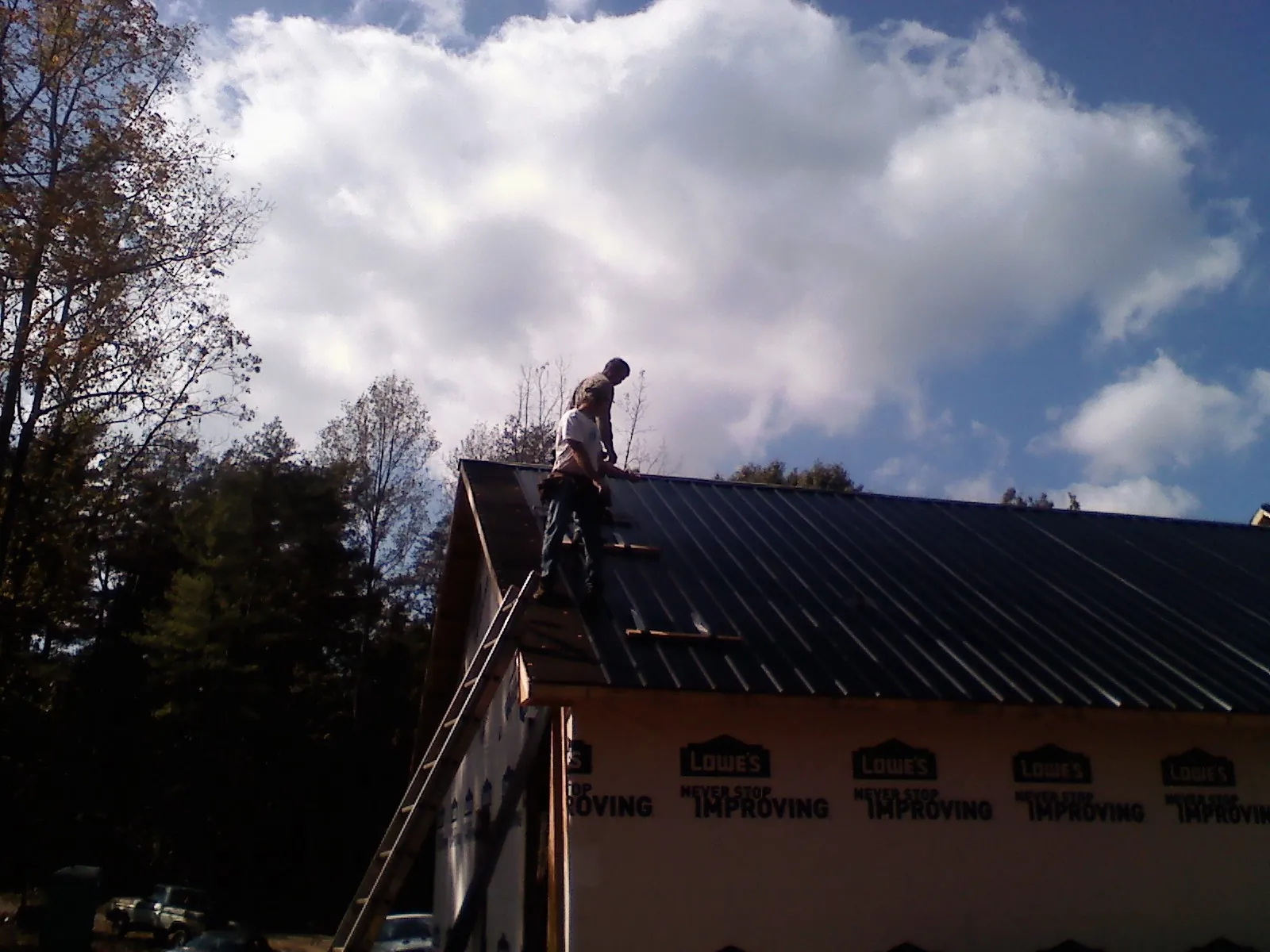 Roofer fastening dark metal panels high against a cloudy sky, from a Roof Inspection job in Blacklick