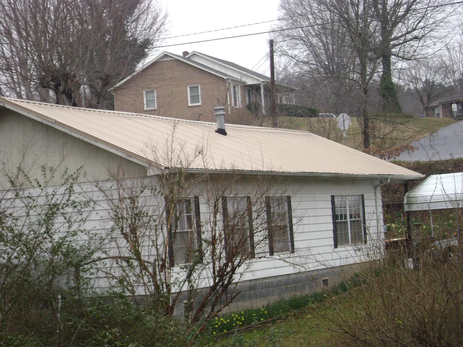 Tan metal roof on a white sided house set into a hillside — Commercial Roofing by Roofing Brothers in Blacklick